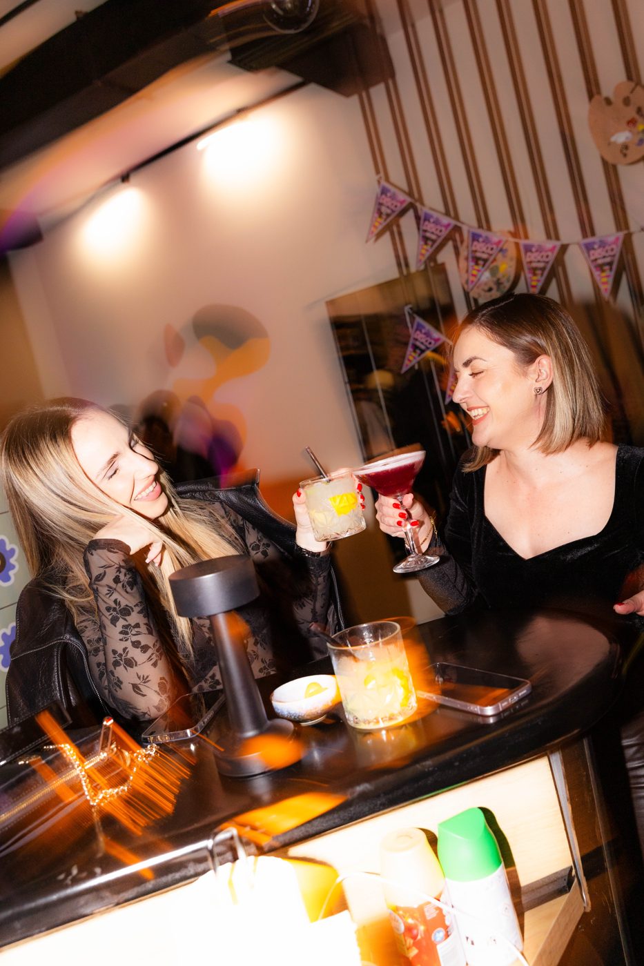 Two friends laughing and toasting cocktails at RABOTEKA